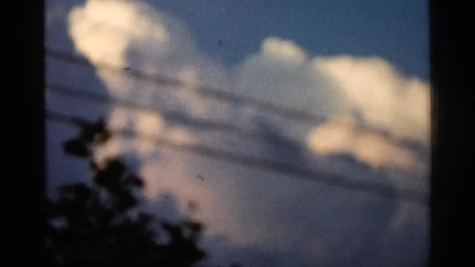 1966 Hamel, Minnesota 8mm frame showing blurred white clouds, blue sky, utility lines, and dark leafy silhouettes near the bottom.