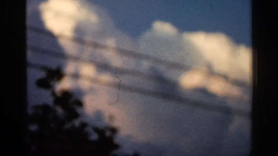 1966 Hamel, Minnesota 8mm frame with cumulus clouds, horizontal utility lines, dark tree silhouettes, and visible film dust.