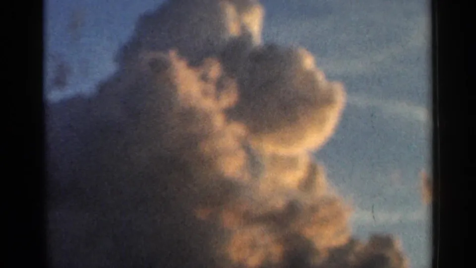 1966 Hamel, Minnesota 8mm frame of a glowing cumulus cloud with blue sky and a faint treetop silhouette below.