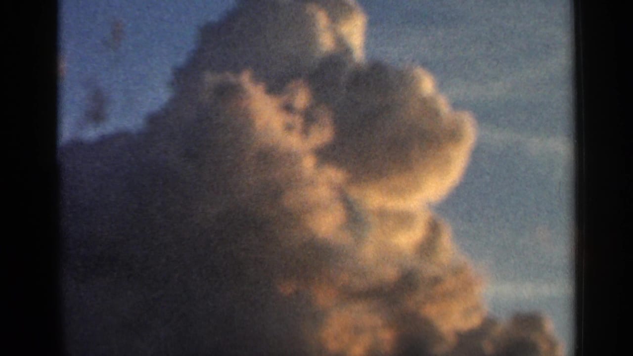 1966 Hamel, Minnesota home-movie frame showing a warm-lit cumulonimbus-like cloud rising against blue sky.