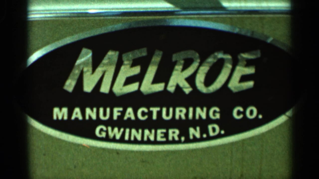 Close-up of a black oval Melroe Manufacturing Co. sign on a metal surface.