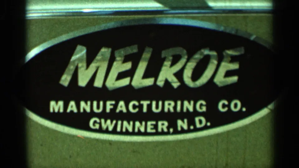 1966 Hamel, Minnesota home-movie frame showing a close-up Melroe Manufacturing Co. sign with Gwinner, N.D. lettering.