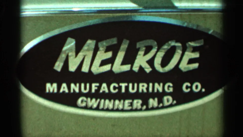Tight home-movie frame showing Melroe Manufacturing Co. and Gwinner, N.D. text on the sign in the 1966 Hamel clip.