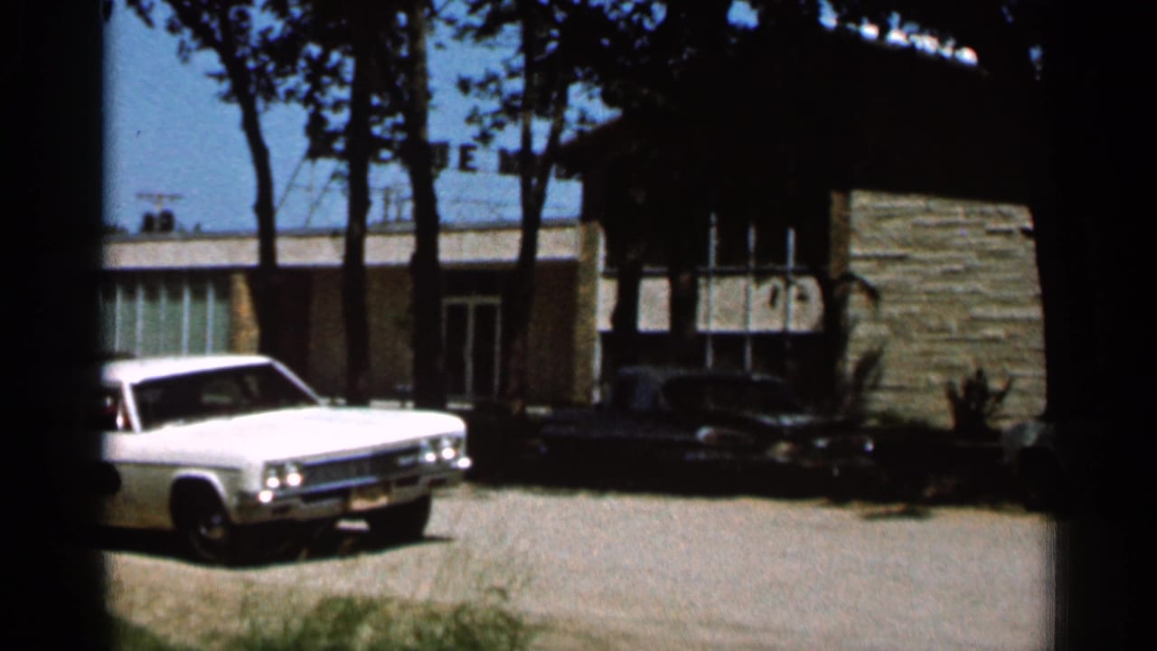 White sedan partly left of frame with a dark car parked near a stone-faced building.