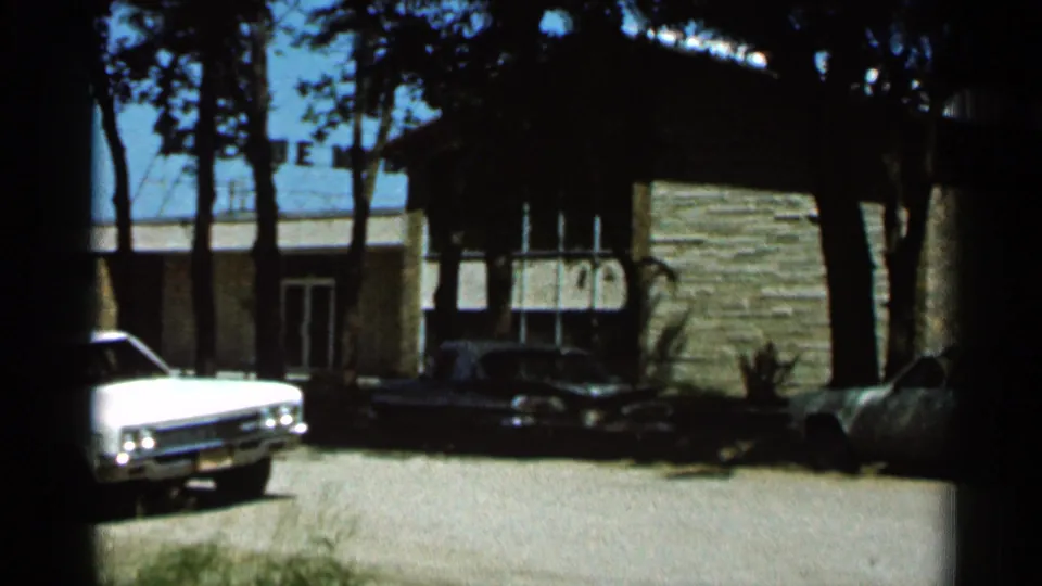1966 Hamel, Minnesota 8mm still showing the white car moving out of frame as the building, trees, and dark car remain visible.