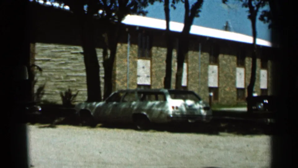 1966 Hamel, Minnesota frame showing a stationary light wagon, stone building wall, white doors, and deep tree shade.