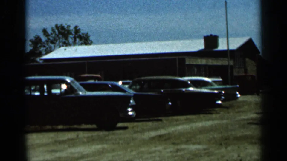 1966 Hamel, Minnesota frame with several mid-century cars lined up along a gravel area outside a brick building.