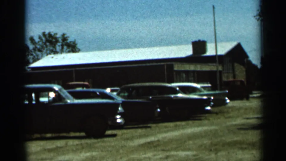 1966 Hamel, Minnesota frame showing mid-century cars parked outside a brick low-rise building with visible 8mm edge darkening.