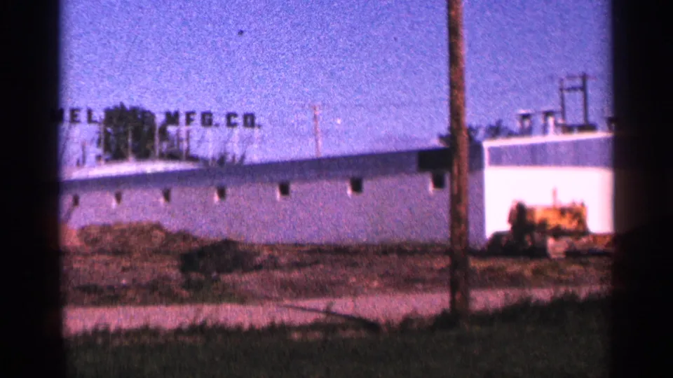 1966 Hamel, Minnesota 8mm frame showing a white warehouse with a MELROSE MFG. CO. rooftop sign beside a dirt work yard.