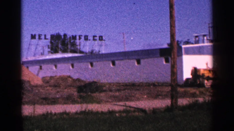 1966 Hamel, Minnesota view of the Melrose manufacturing building with a foreground pole, dirt piles, and yellow construction equipment.