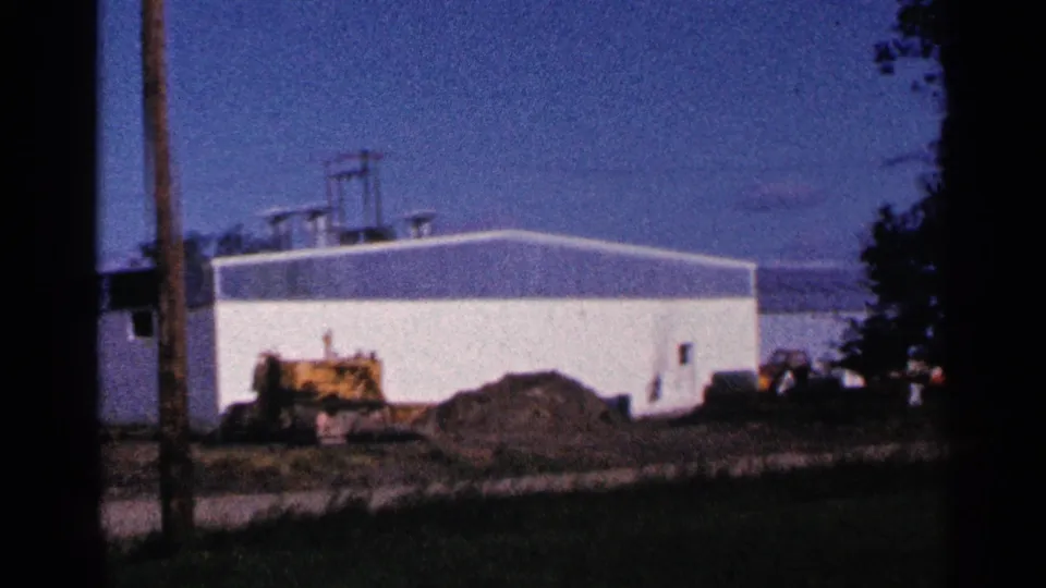 White industrial building in Hamel, Minnesota, with construction equipment and utility poles visible in a grainy 1966 8mm frame.