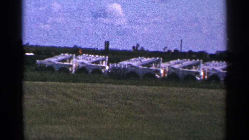 1966 Hamel, Minnesota frame showing rows of white farm or industrial equipment in a grassy field near low structures.