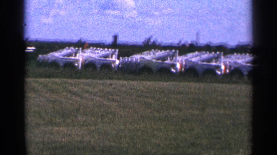 1966 Hamel, Minnesota frame with white agricultural equipment lined across open grass and a distant dark tree line.