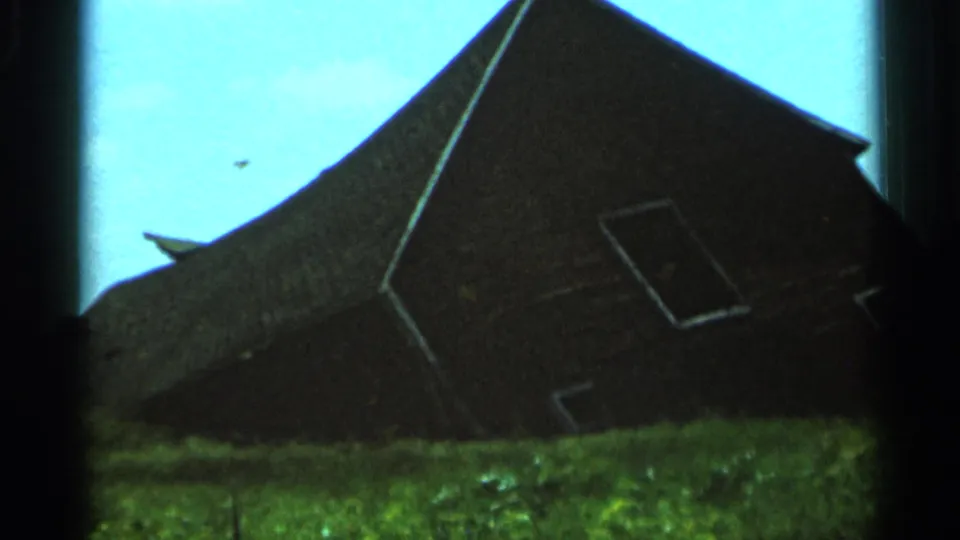 1966 Hamel, Minnesota home-movie frame showing a dark barn with a steep roof, small windows, and bright sky behind it.