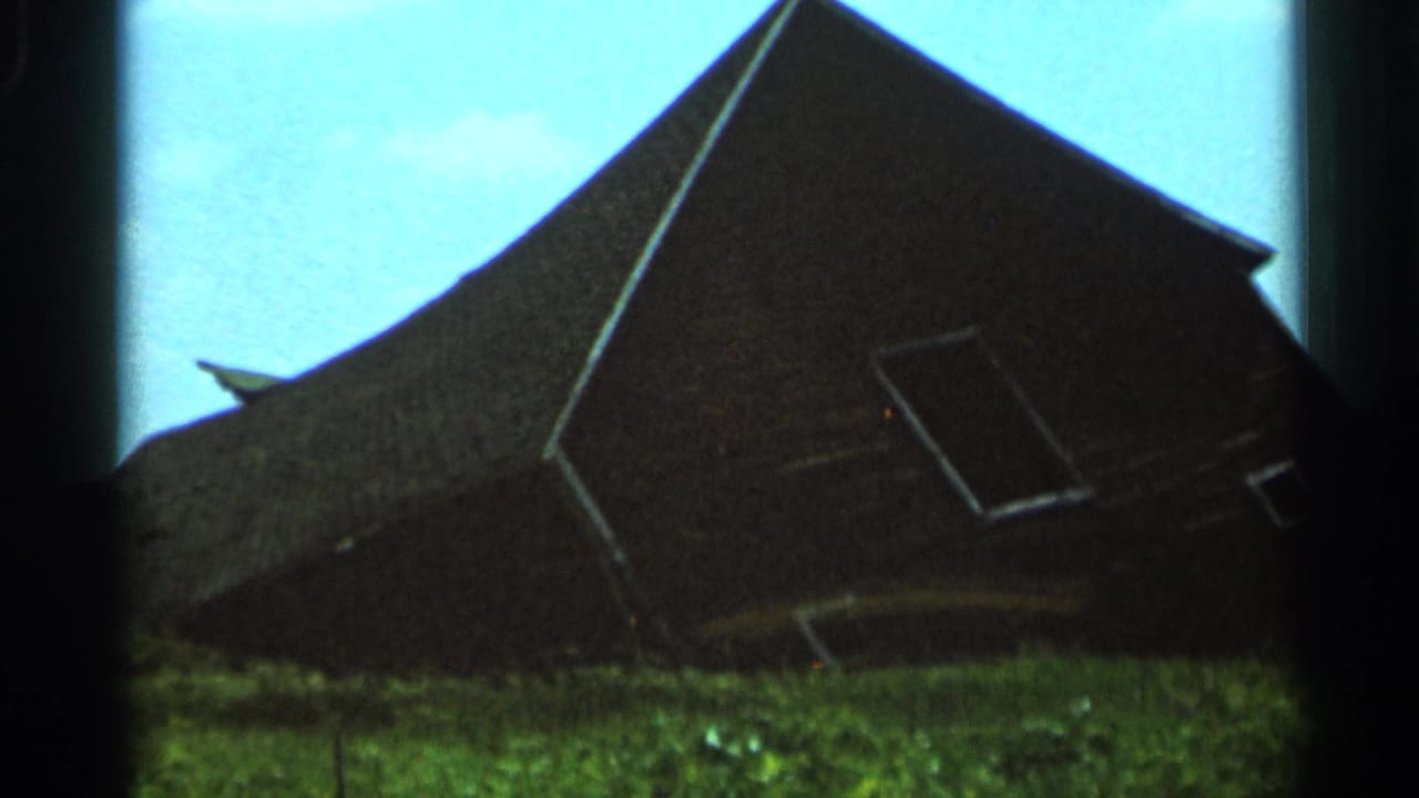 1966 Hamel, Minnesota 8mm frame showing a dark weathered barn with a steep roof against bright blue sky and grass.