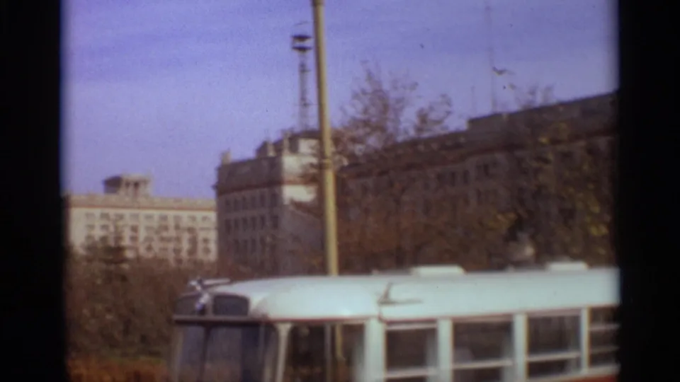 1966 Moscow street view with a white bus in the foreground, autumn trees, and a large Soviet-era building behind it.