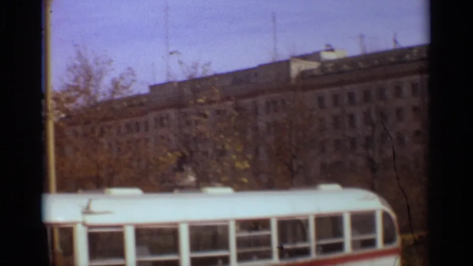 1966 Moscow urban frame showing a white bus, autumn trees, and a broad masonry building under a pale sky.