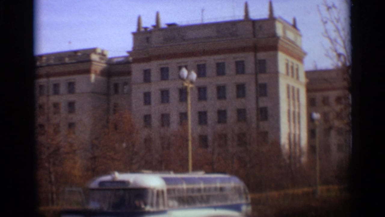 1966 Moscow street view with a large institutional building, bare trees, lamps, and a bus crossing the lower frame.