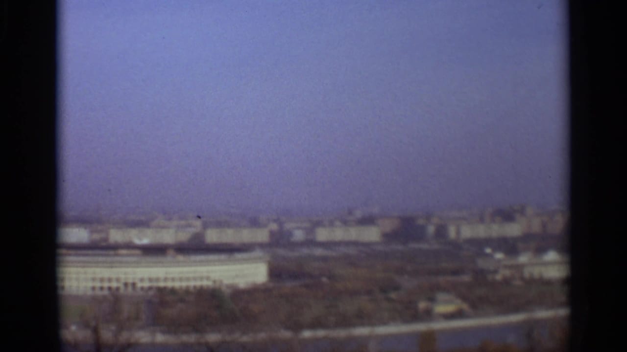 Elevated city panorama with broad buildings, distant skyline, and dark vertical frame edge.