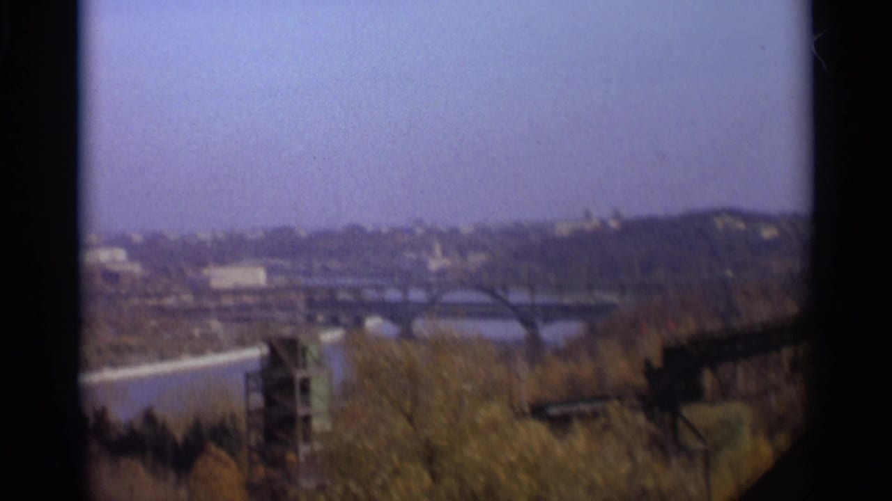 Wide soft-focus skyline with river, bridge arches, trees, and distant structures.
