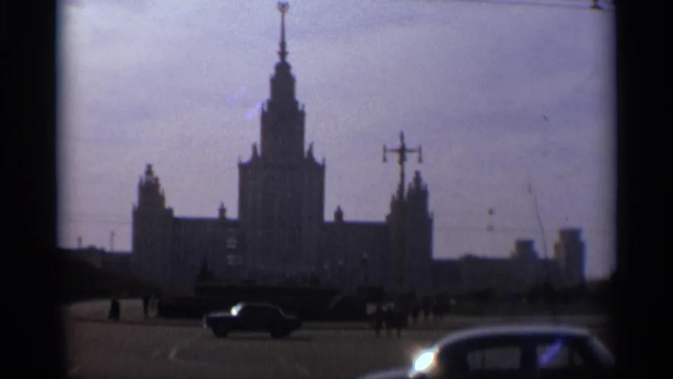 1966 Moscow street-level frame showing a tall spired Soviet-era building, cars, and distant pedestrians in a public space.
