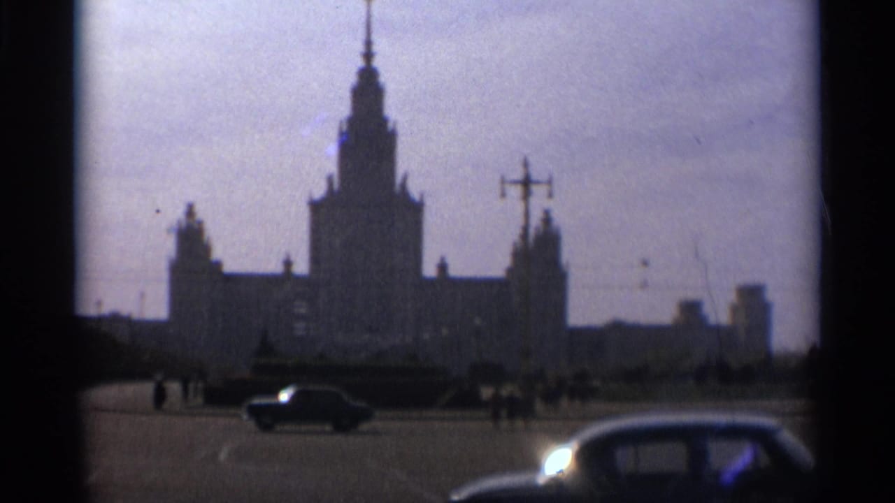 Silhouetted Moscow tower behind a broad street with cars and small pedestrians.