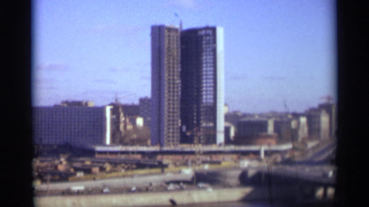 Tall modern high-rise under construction with cranes and city roads below.