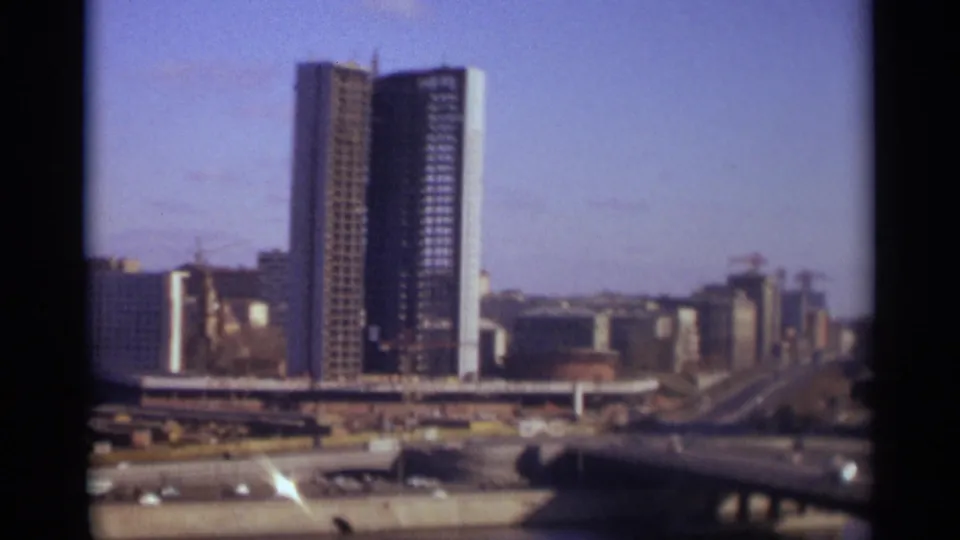 1966 Moscow elevated view with a partly finished high-rise, cranes, surrounding roads, and city blocks fading into the distance.