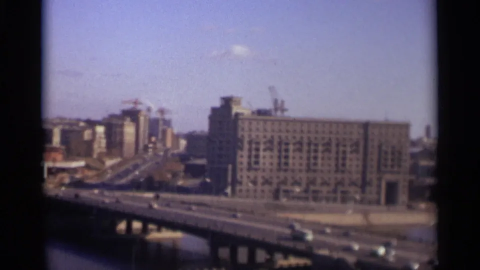 1966 Moscow frame showing cars on a bridge over water, with a broad urban building and construction cranes behind it.