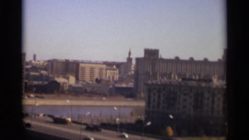 1966 Moscow frame with riverfront traffic in the foreground and large urban buildings across the water.