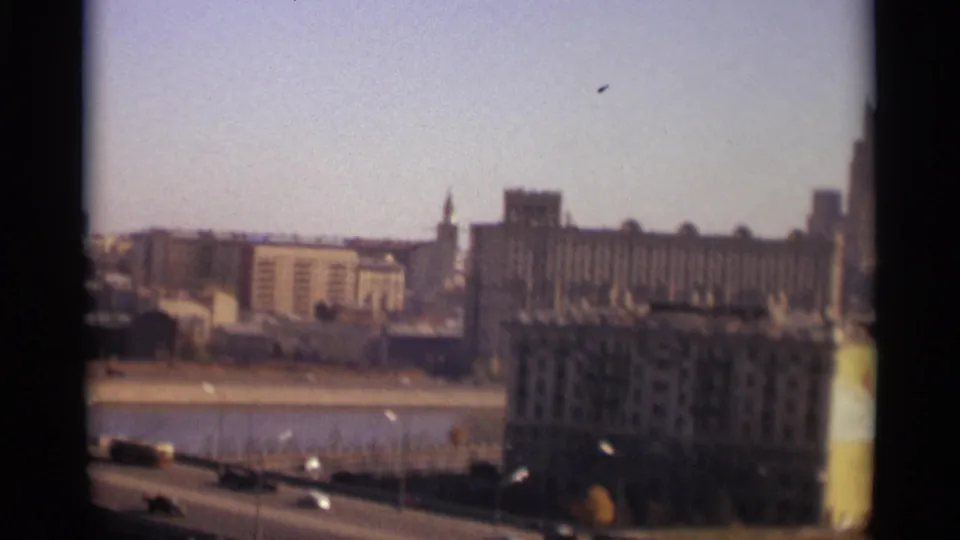 1966 Moscow home-movie frame showing cars along a riverside road and large buildings beyond the river.