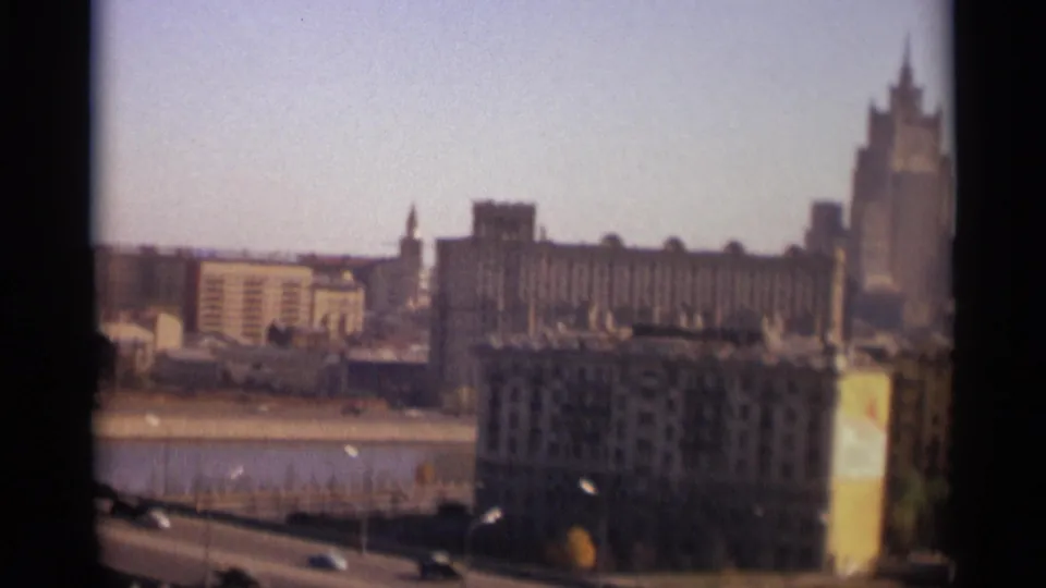 1966 Moscow frame showing the riverfront road, large foreground building, and a tall distant high-rise during a city pan.