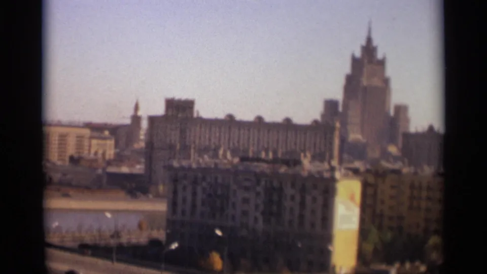 End frame of a 1966 Moscow skyline view, with cars on a lower roadway, a river at left, and a tall Stalinist-style building in the distance.