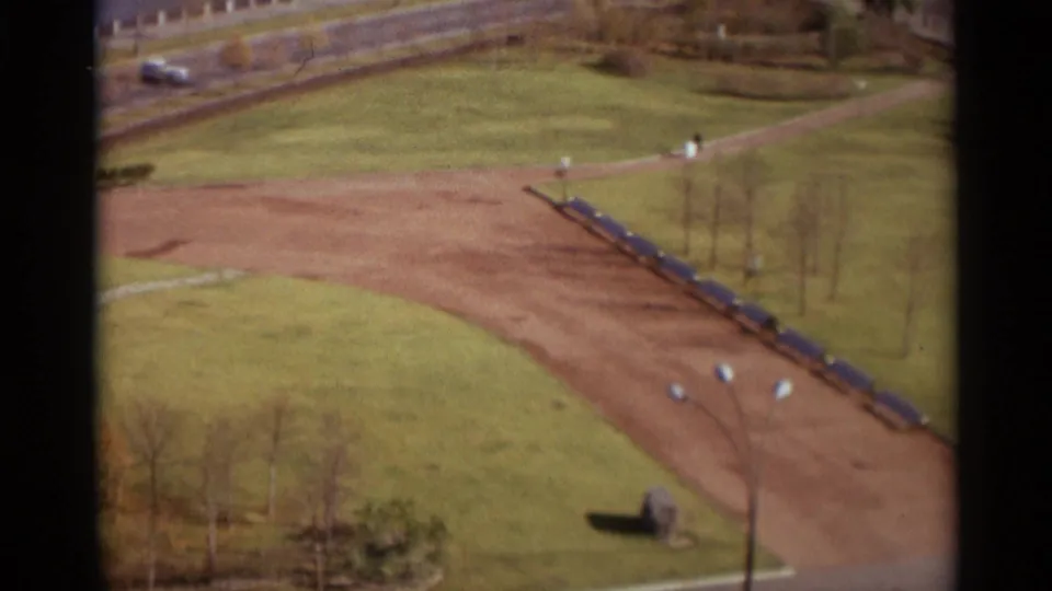 1966 Moscow home-movie still with a high view over lawns, a sweeping dirt path, road, small pedestrians, and sparse trees.