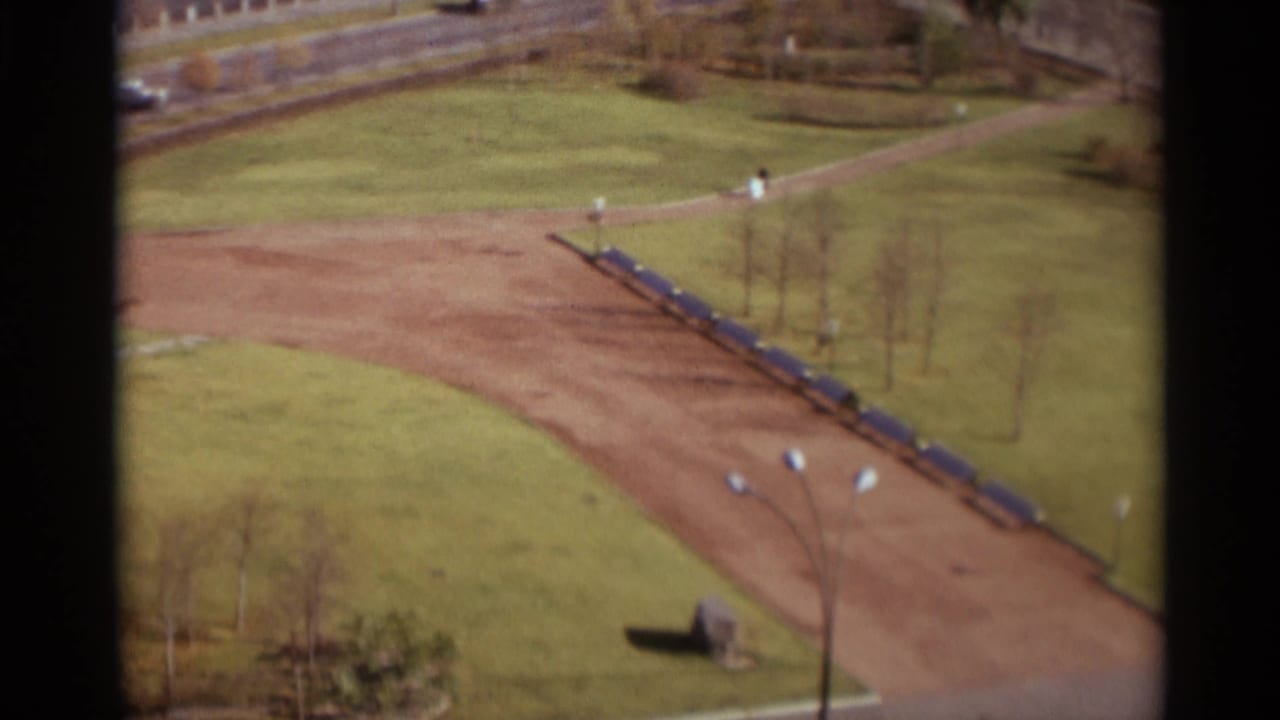 Elevated view of a park path with blue benches, lawns, bare trees, and a few distant pedestrians.