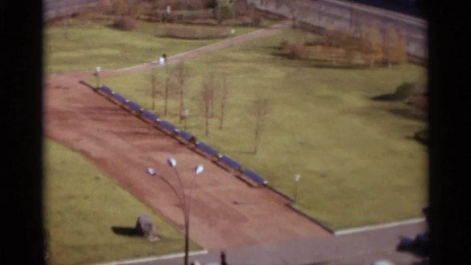 1966 Moscow park frame showing the bench-lined dirt path, green grass, streetlights, and small pedestrians near the road edge.