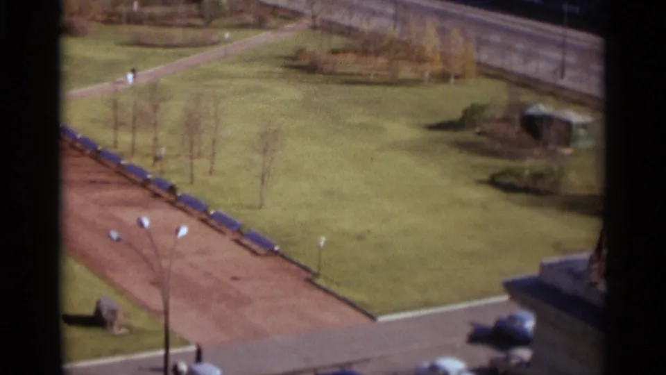 Elevated 1966 Moscow park view with blue benches, open lawn, a few pedestrians, and partial structures at the frame edge.