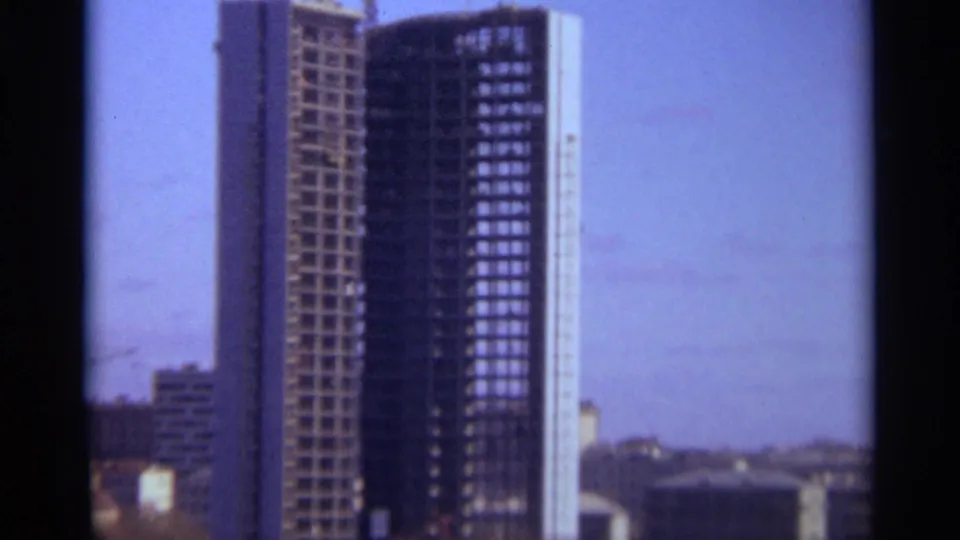 1966 Moscow 8mm frame of a tall high-rise under construction, with exposed facade bays and lower buildings in the distance.