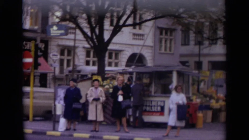 1966 Moscow street scene with women in coats near a small kiosk, flower display, and light-colored building facade.