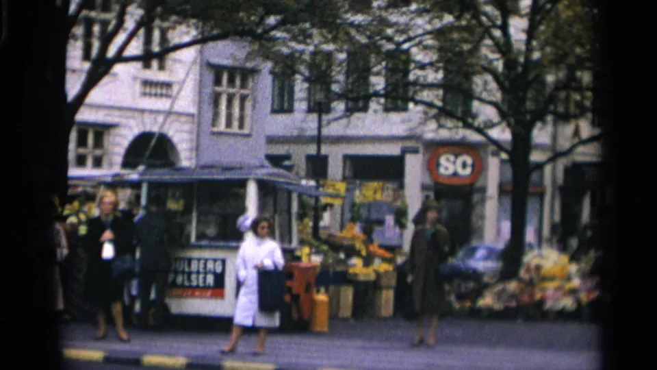 1966 Moscow home-movie frame of women on a sidewalk beside a flower stall, kiosk, trees, and light-colored building frontage.