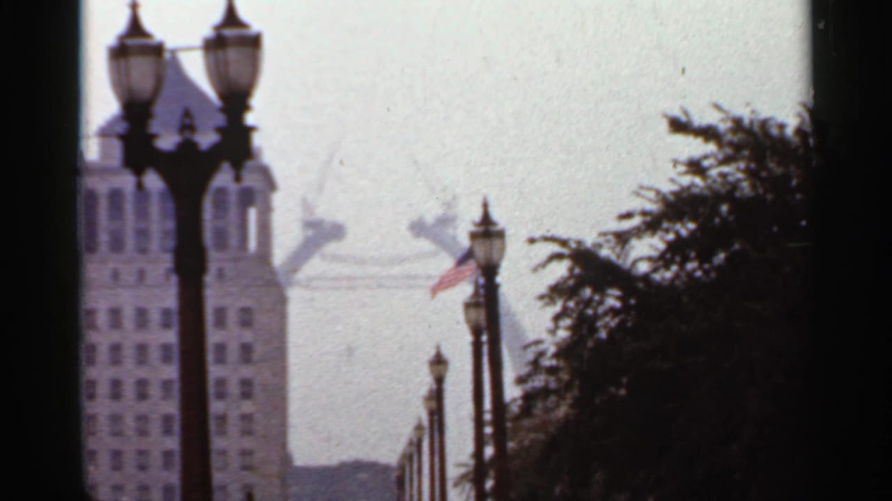 Streetlamps frame a tall city building with an American flag and hazy Gateway Arch behind it.