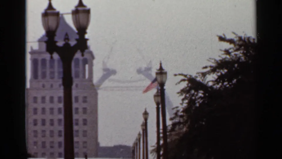 Saint Louis street view from 1966 showing a tall building, American flag, trees, streetlamps, and the Gateway Arch in the distance.
