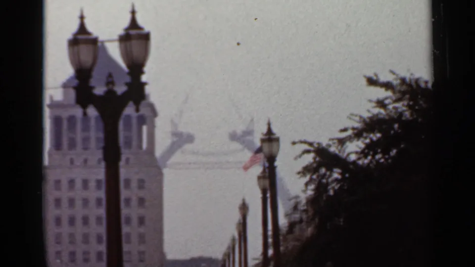 1966 Saint Louis footage holds on streetlamps, a tall building, an American flag, trees, and the hazy Gateway Arch beyond.