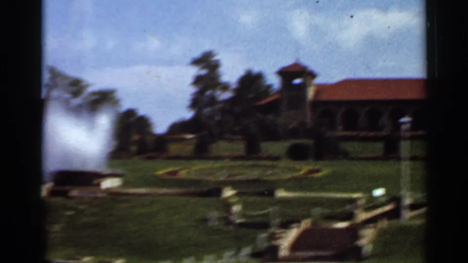 1966 home-movie frame of Grant's Farm grounds with lawn, fountain spray and a red-roofed building in the distance.