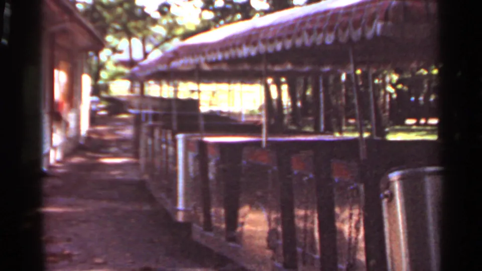 Visitor walkway or platform at Grant's Farm, with a long covered roof, railings, bins, and shaded pavement in 1966 home-movie footage.