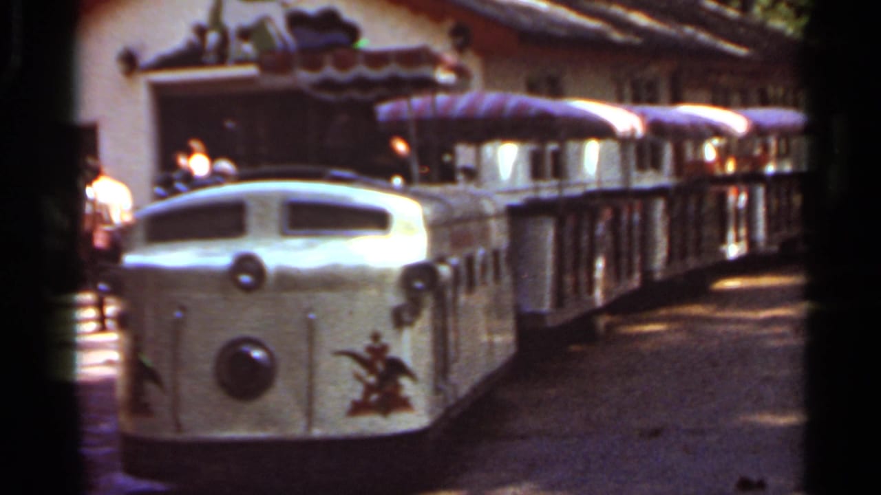 1966 Saint Louis home-movie frame showing a cream miniature amusement train with striped canopy passenger cars.