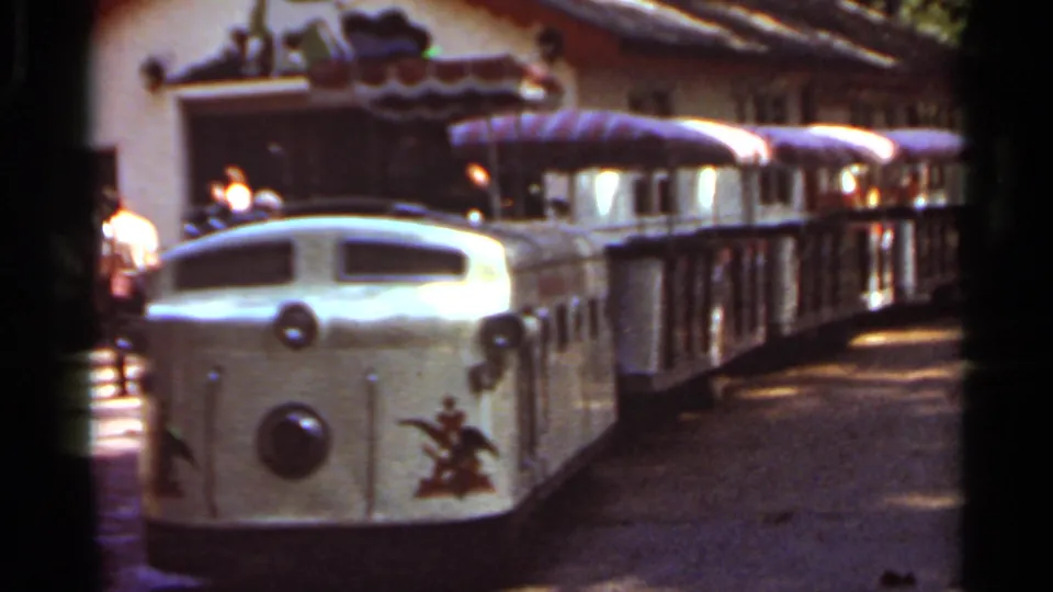 1966 Saint Louis home-movie frame showing a cream miniature amusement train with striped canopy passenger cars.