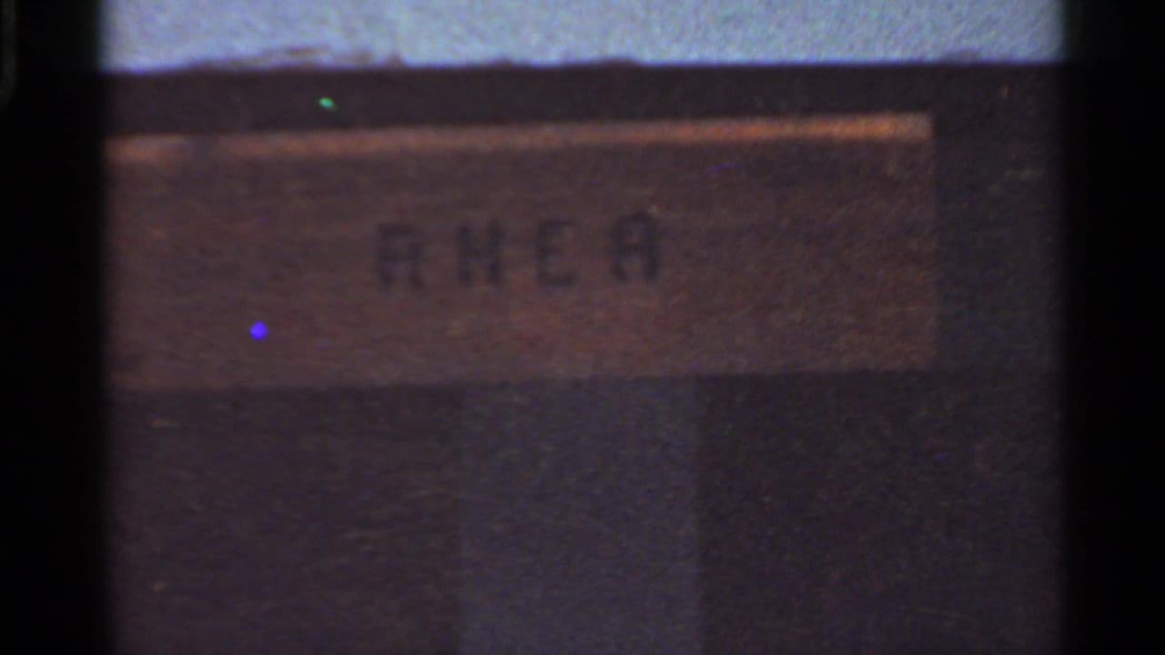 Blurred enclosure sign or placard seen through dark film-frame borders.