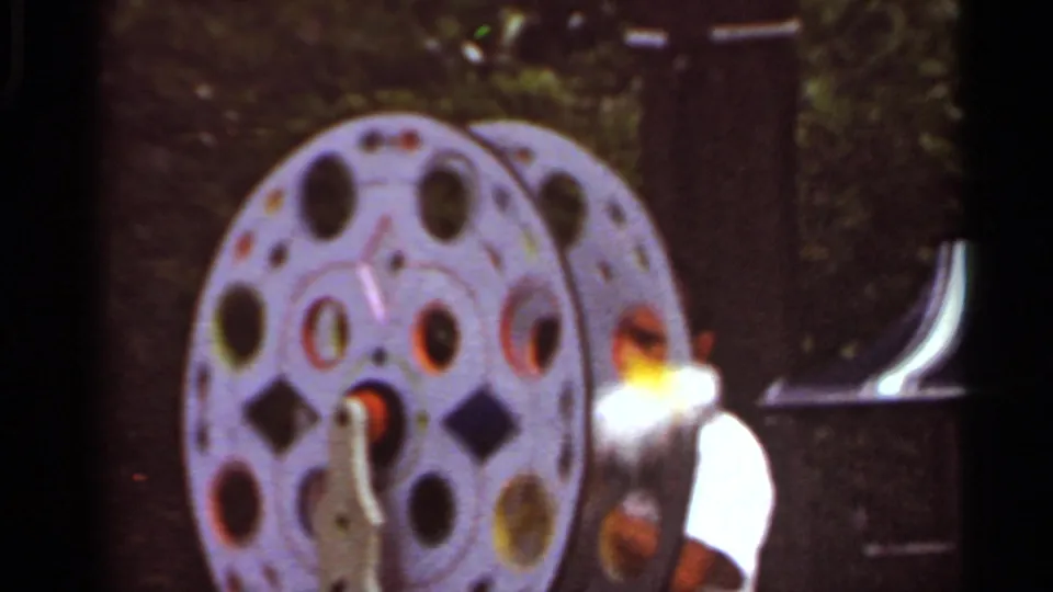 White cockatiel with a yellow head perched beside a circular metal stand in 1966 Saint Louis home-movie footage.