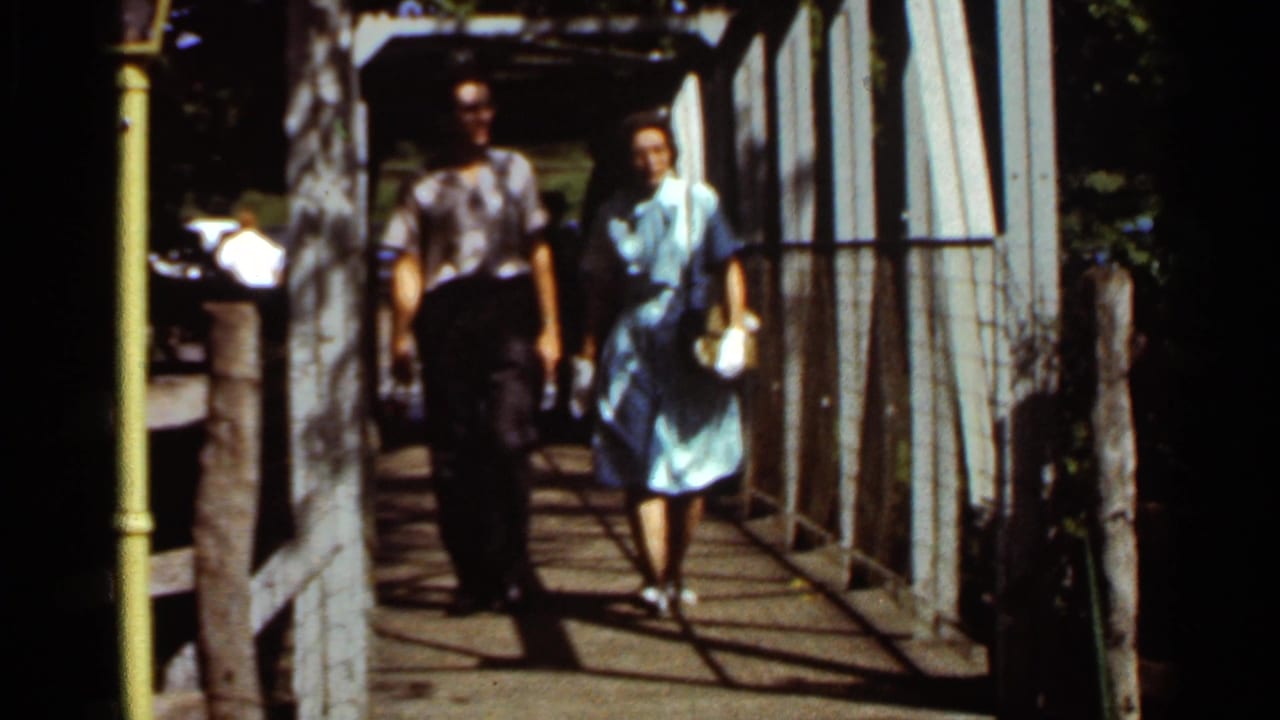 Older couple walking toward the camera on a wooden pedestrian bridge.